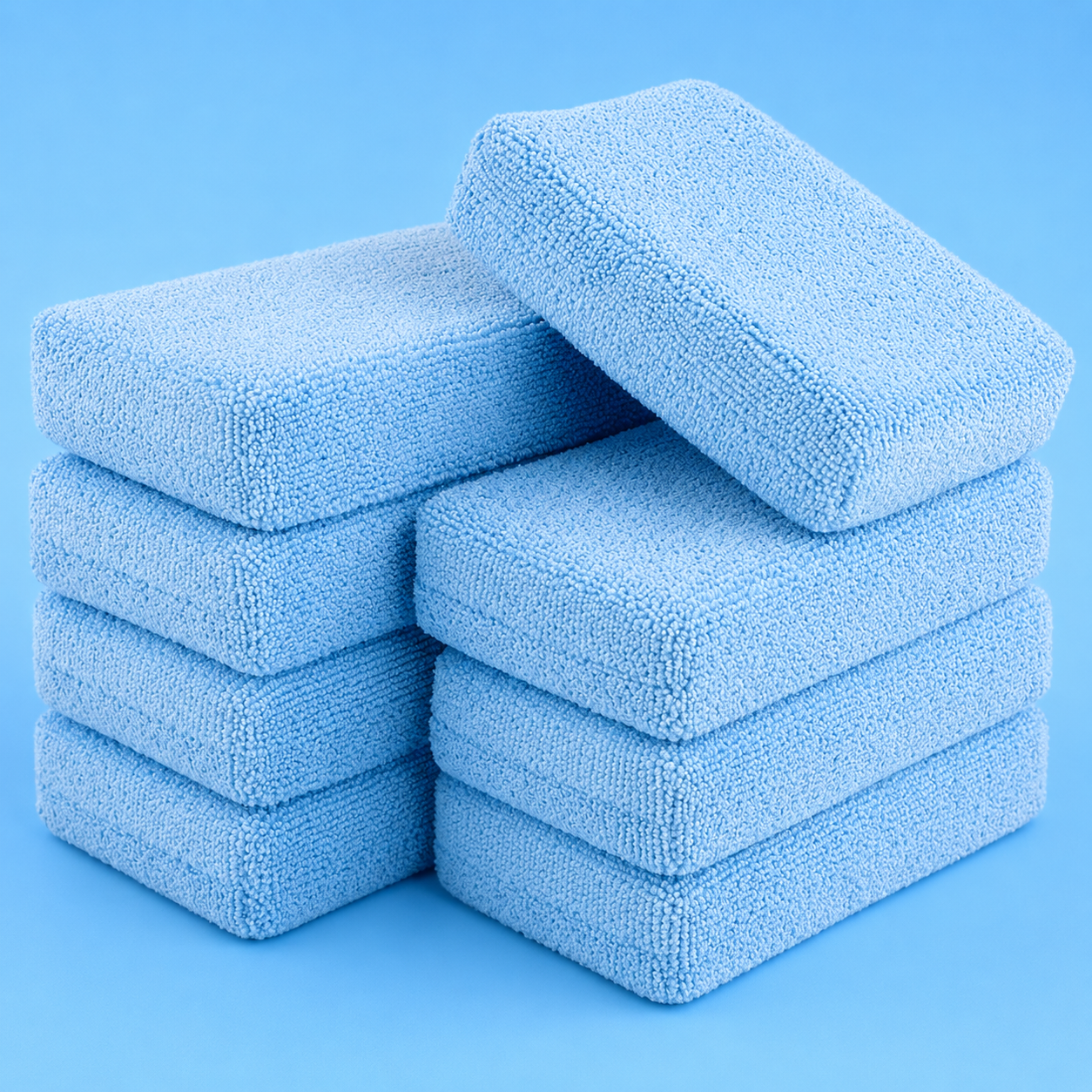 A stack of rectangular, light blue microfiber car wash sponges arranged against a solid blue background.