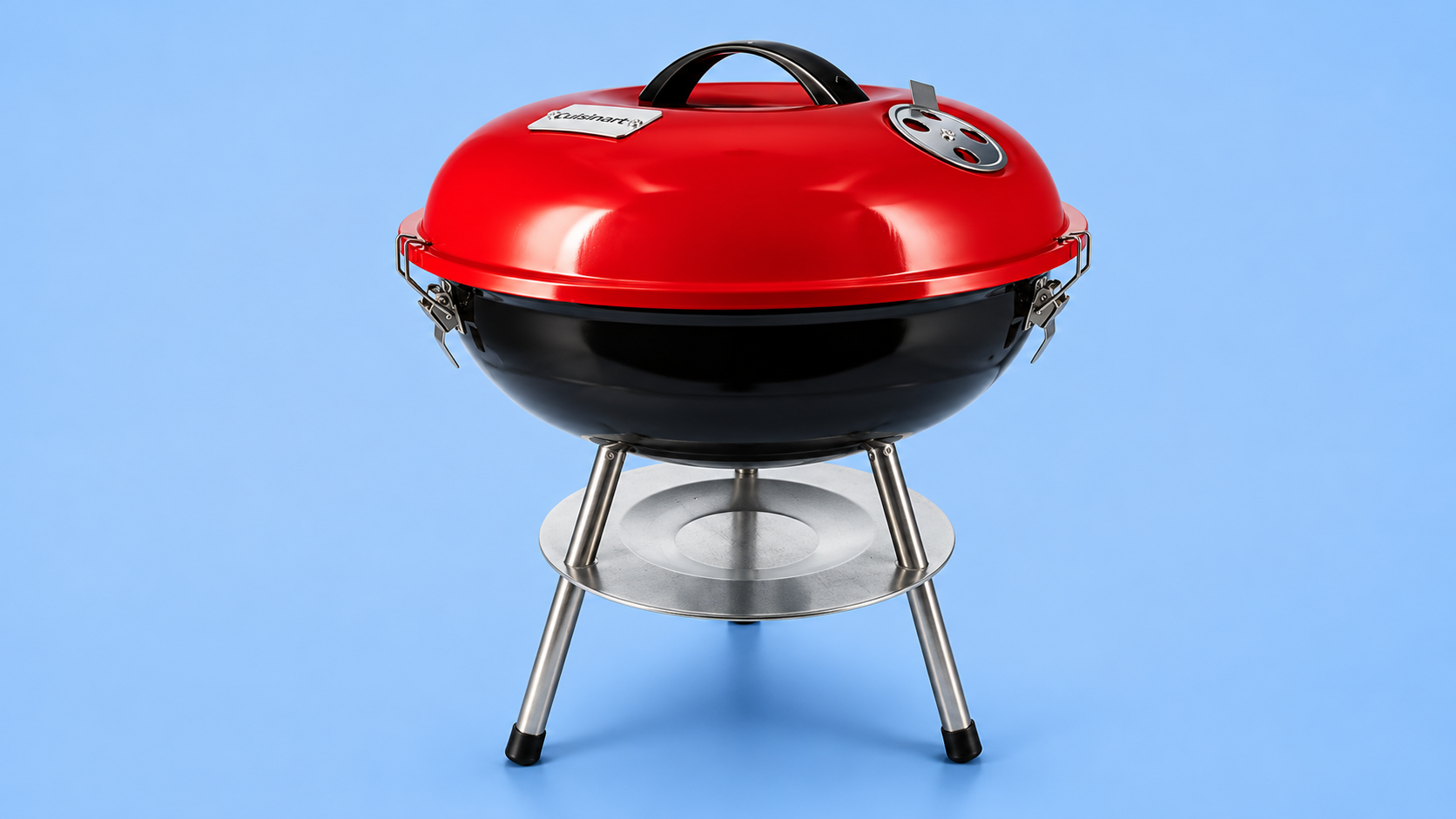 A red and black Cuisinart portable charcoal kettle grill against a blue background.