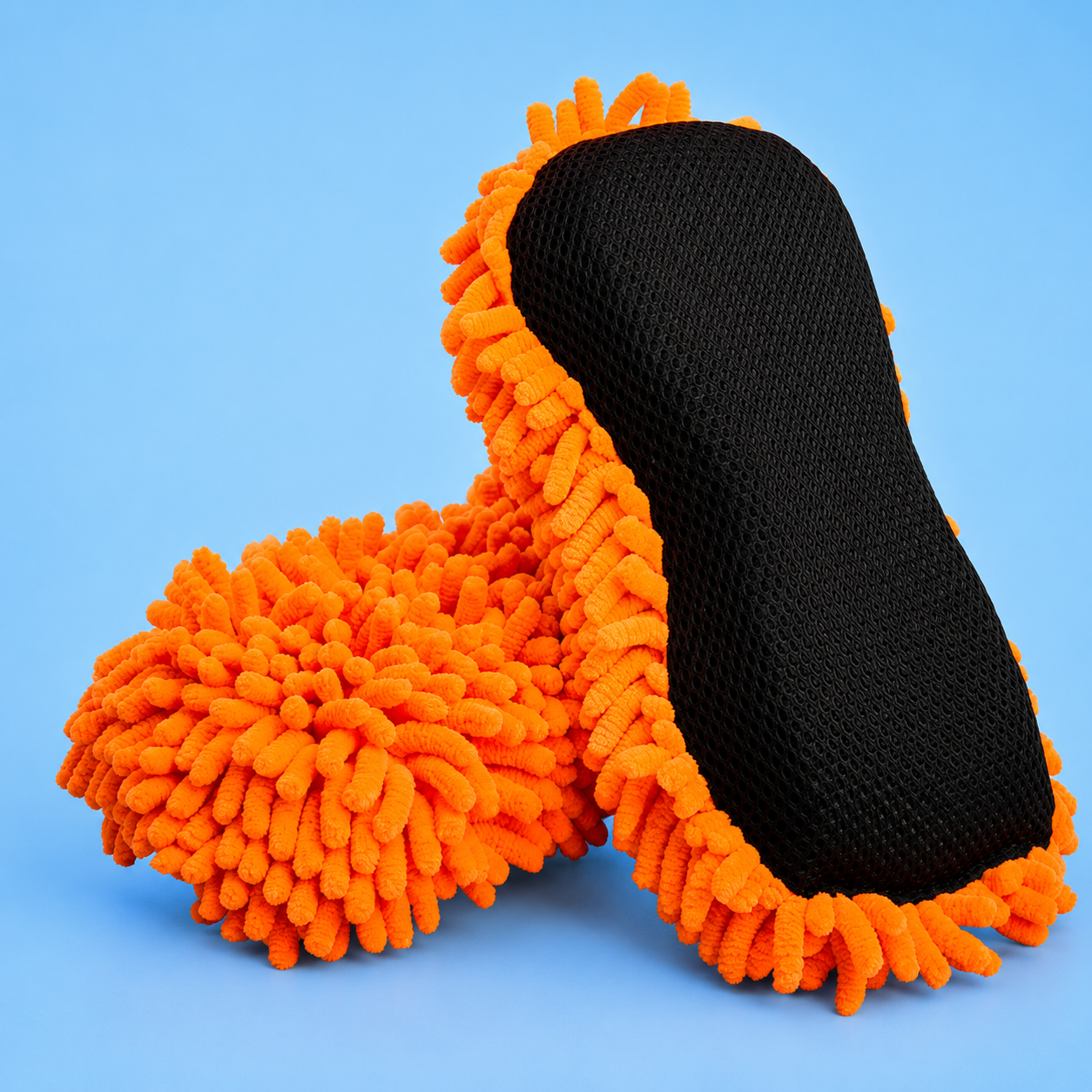 Two orange chenille microfiber car wash sponges, showing one flipped over to display its black mesh scrubbing backing on a solid blue background.