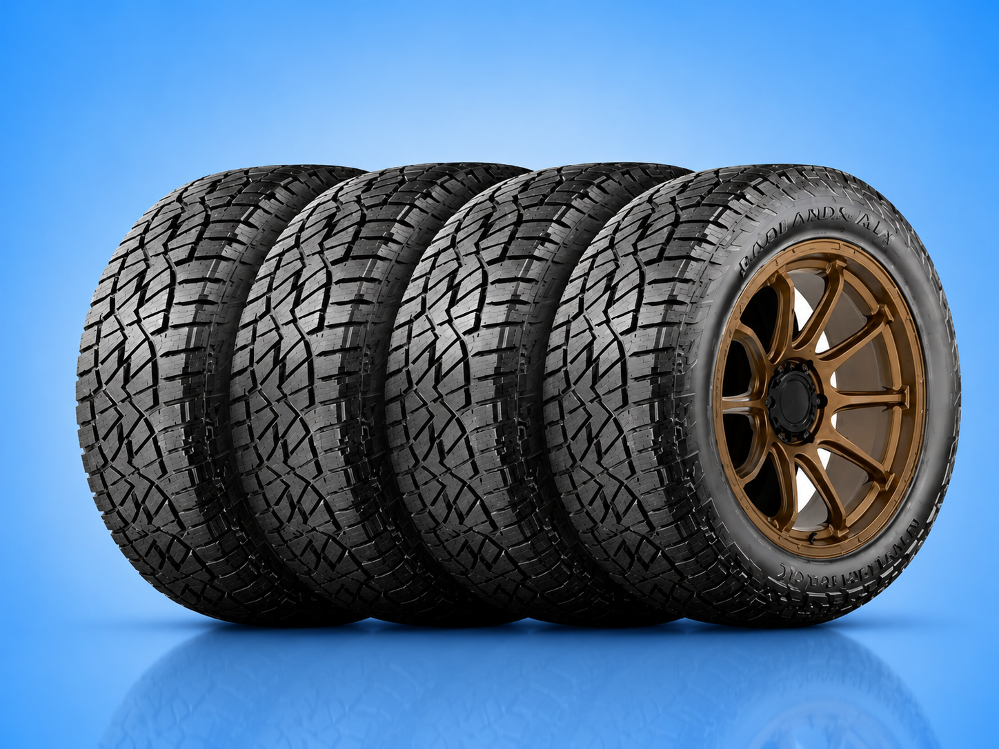 Set of four Badlands ATX all-terrain truck tires with bronze rims against a solid blue background.